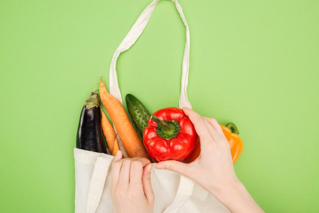 частичный вид женщины положить красочный перец колокольчик в хлопчатобумажный мешок с овощами на светло-зеленом фоне
 - Фото, изображение