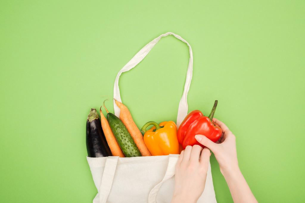 vue recadrée de la femme mettant des légumes colorés dans un sac de coton sur fond vert clair
 - Photo, image