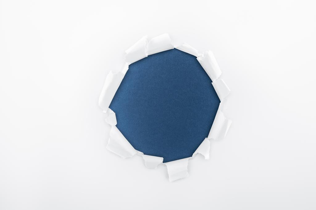 zerlumptes Loch in strukturiertem weißem Papier auf dunkelblauem Hintergrund  - Foto, Bild