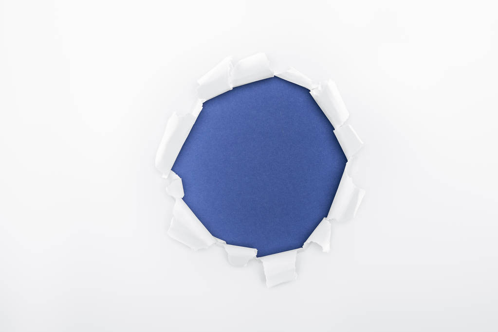 torn hole in textured white paper on blue background  - Photo, Image