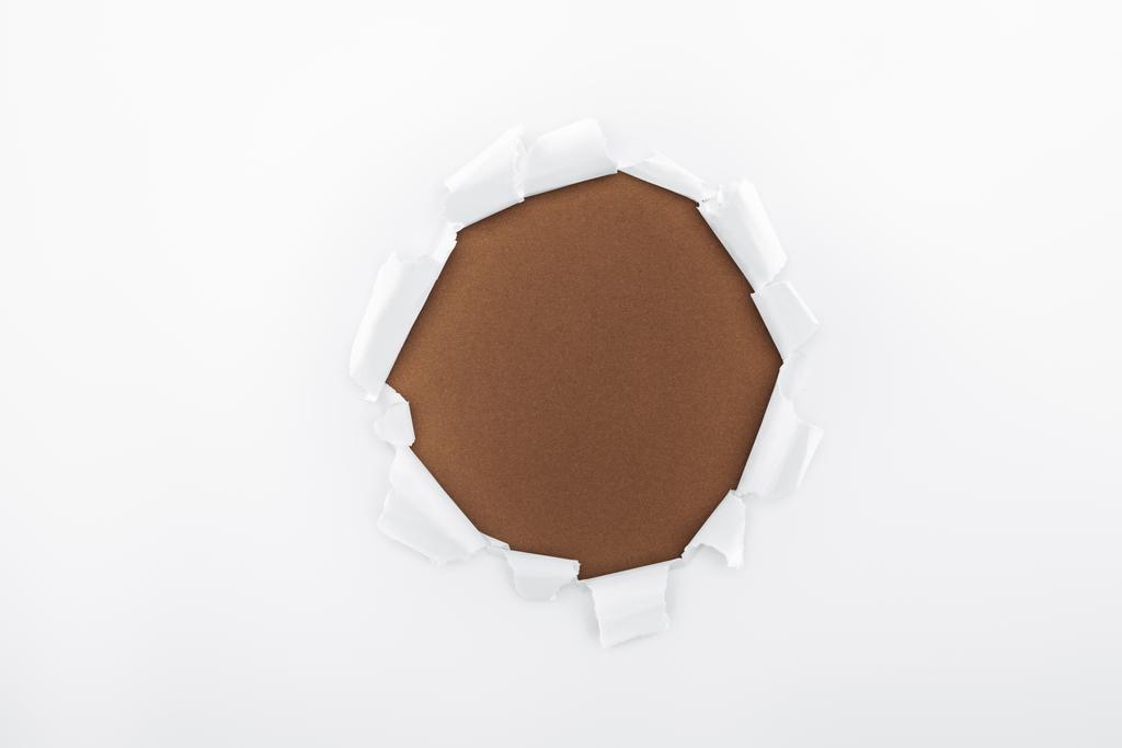 zerrissenes Loch in weißem strukturiertem Papier auf braunem Hintergrund  - Foto, Bild