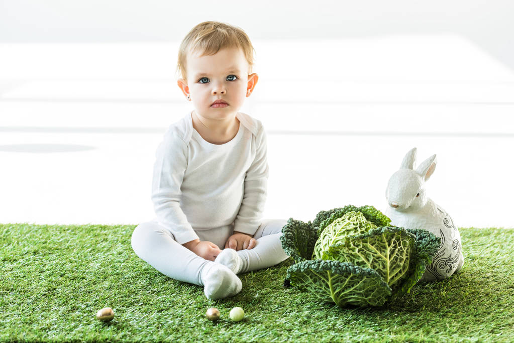 roztomilé miminko v blízkosti zelí Savojského, ozdobného králíka a barevných křepelových vajec na bílém - Fotografie, Obrázek