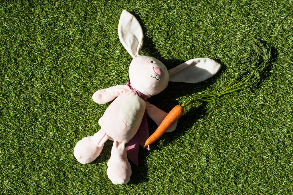 top view of toy rabbit and fresh carrot on green grass surface - Photo, Image