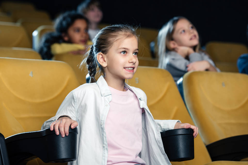 προσεκτικός χαμογελώντας παιδιού βλέποντας ταινία στον κινηματογράφο με την πολυπολιτισμική τους φίλους - Φωτογραφία, εικόνα