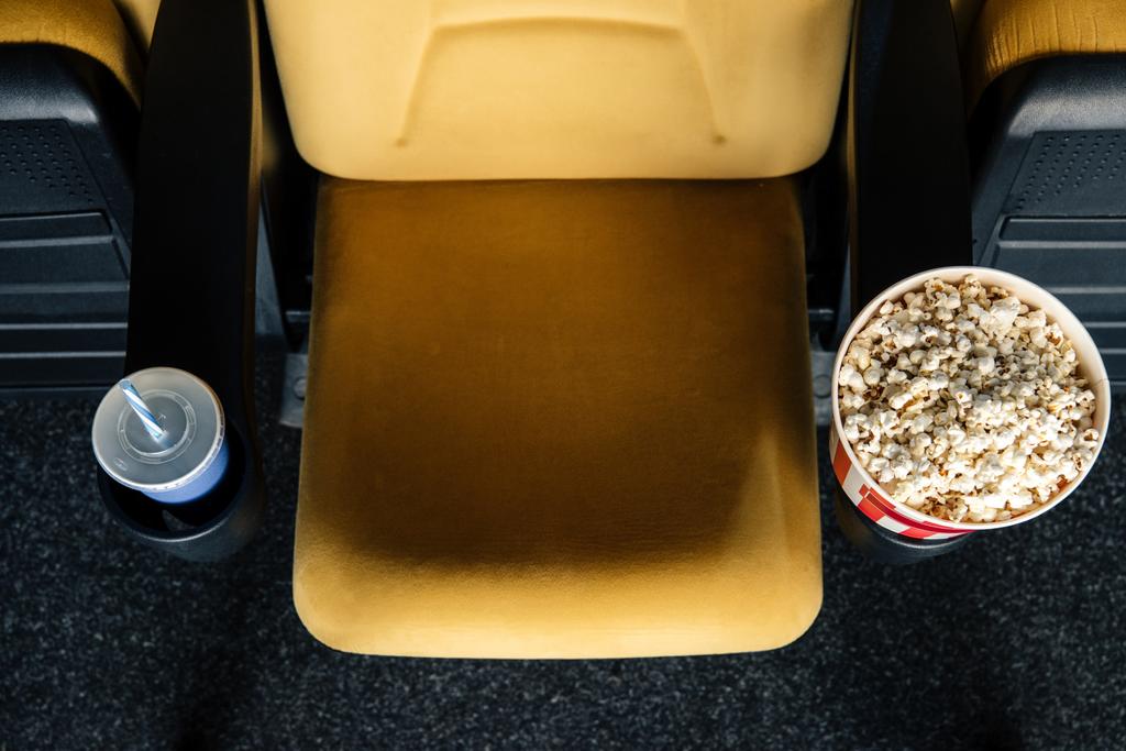 bovenaanzicht van Oranje bioscoop stoel met papieren kopjes soda en popcorn in bekerhouders - Foto, afbeelding