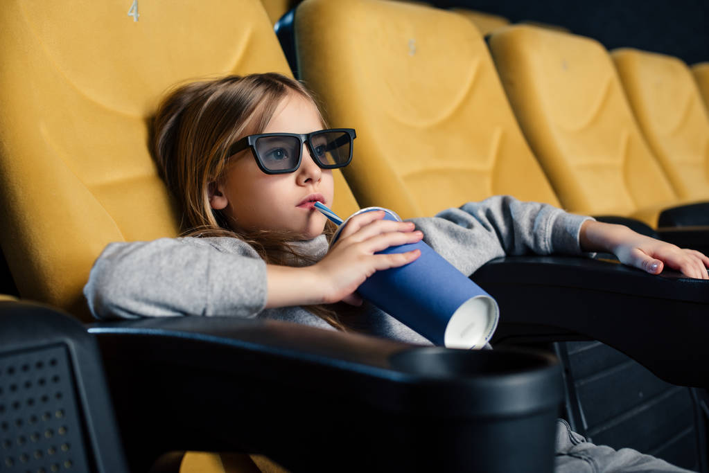 entzückendes Kind in 3D-Brille sitzt im Kino und trinkt aus Pappbecher - Foto, Bild