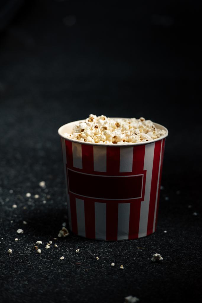 раздетая красно-белая бумажная чашка с попкорном на полу кинозала
 - Фото, изображение
