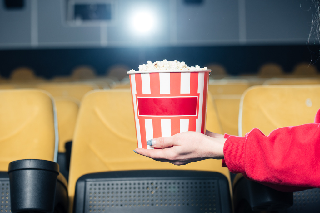 Teilansicht von Kind mit gestreiftem Pappbecher mit Popcorn im Kino - Foto, Bild