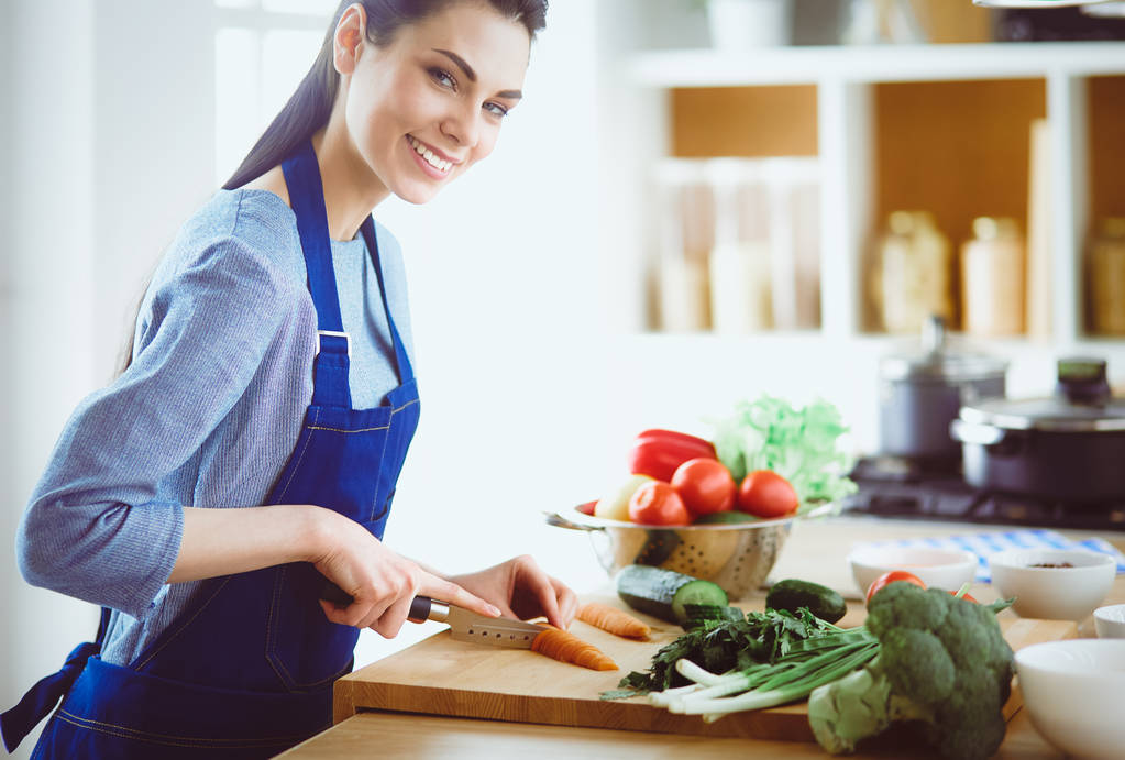 Молодая женщина режет овощи на кухне дома - Фото, изображение