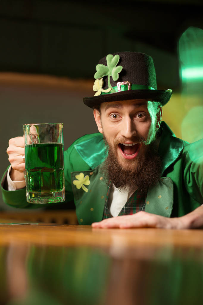 Dark-haired bearded young man in a leprechaun hat with shamrock looking amazed - Photo, Image