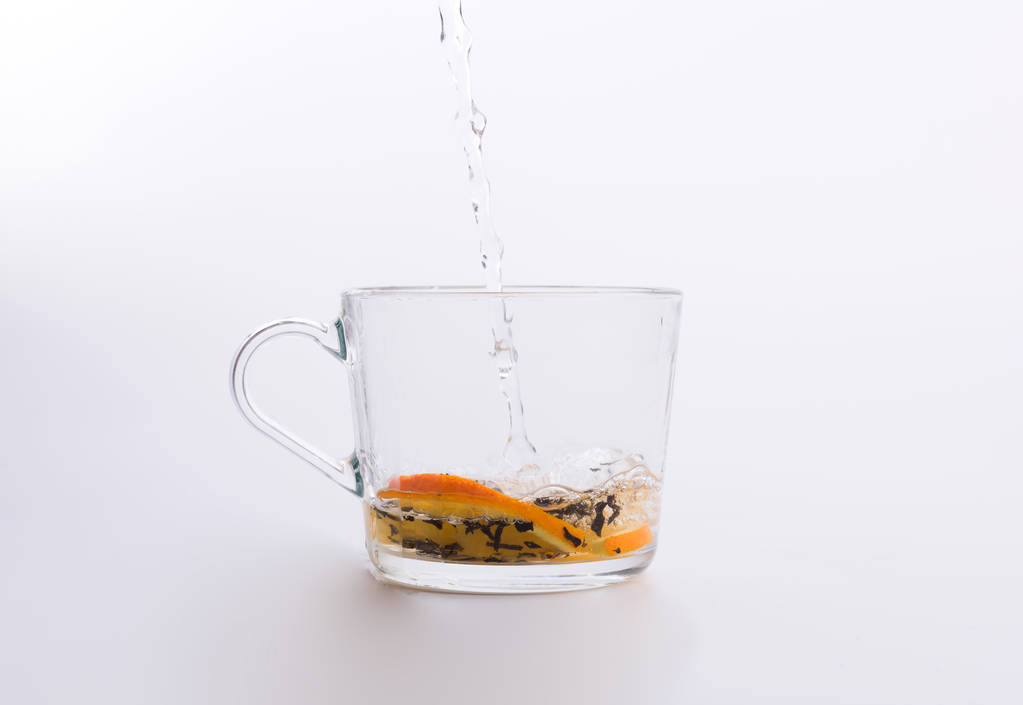 Água derramando em copo de vidro com chá e fatias de laranja isolado em branco
 - Foto, Imagem