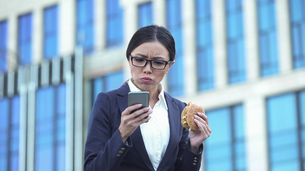 Femme chef de bureau manger hamburger malsain vérifier les messages au téléphone, le stress
 - Photo, image