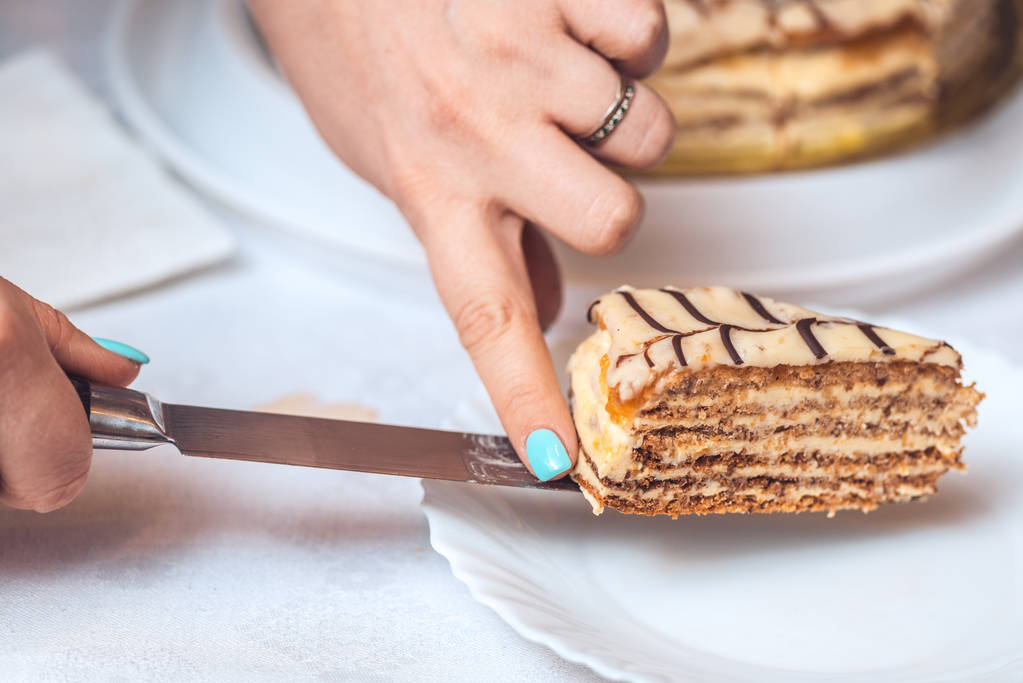 Torta entera esterhazy y una rebanada de pastel en el cuchillo. Las manos de las mujeres lo sostienen. auténtica receta, postre húngaro y austriaco, vista desde arriba, primer plano
 - Foto, imagen