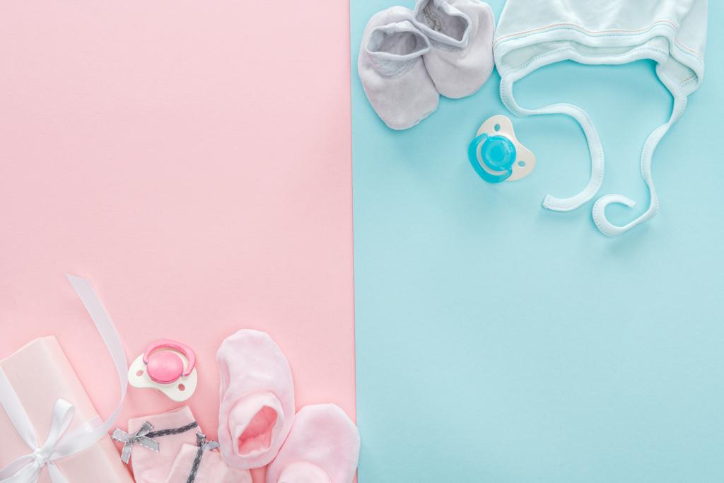 top view of pacifiers, gift, booties, bonnet, socks on pink and blue background - Photo, Image
