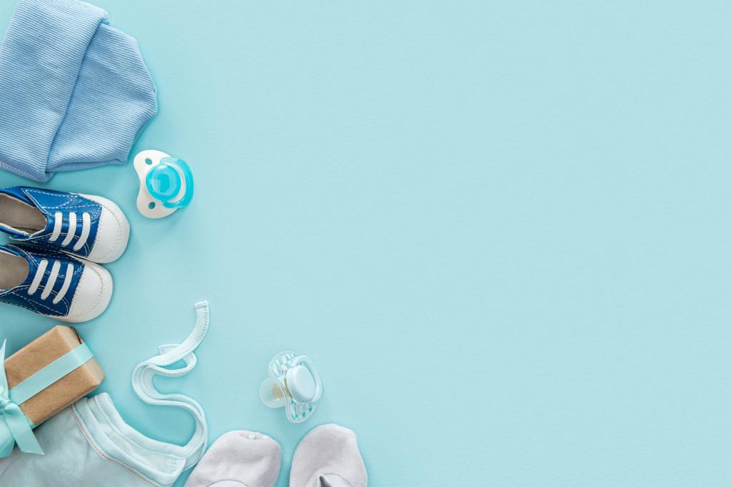 top view of pacifiers, gift, sneakers, bonnet, booties, hat on blue background with copy space - Photo, Image