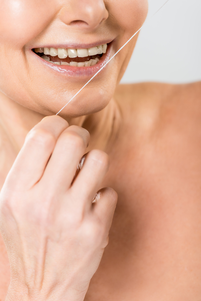 selective focus of mature woman brushing teeth with dental floss isolated on grey - Photo, Image