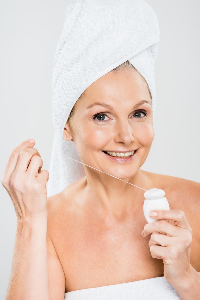attractive and smiling mature woman in towel holding dental floss and looking at camera  isolated on grey - Photo, Image