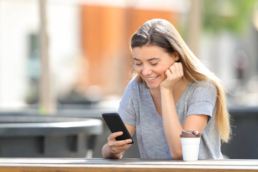 Menina adolescente feliz usando um telefone inteligente sentado em um parque
 - Foto, Imagem