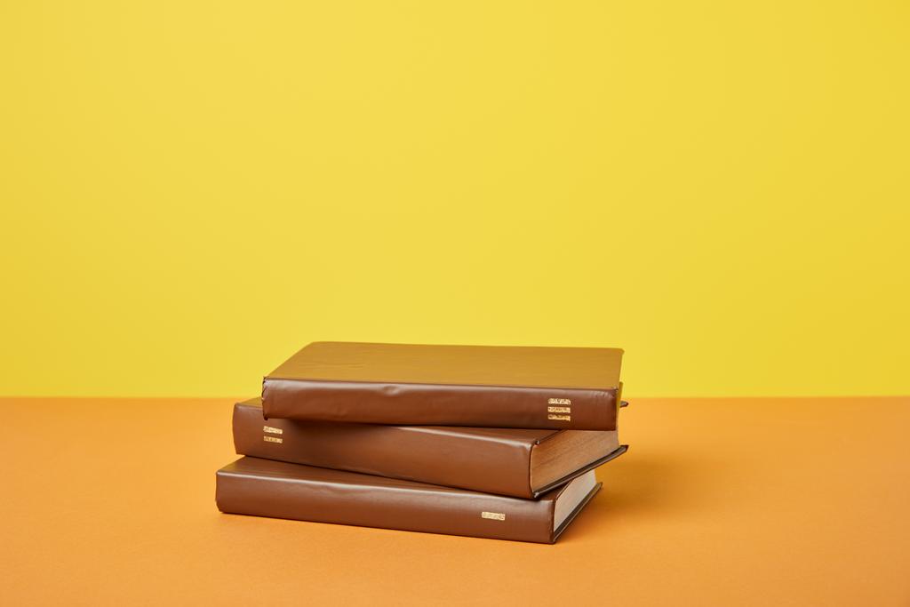 Livros castanhos sobre superfície laranja brilhante isolado em amarelo
 - Foto, Imagem