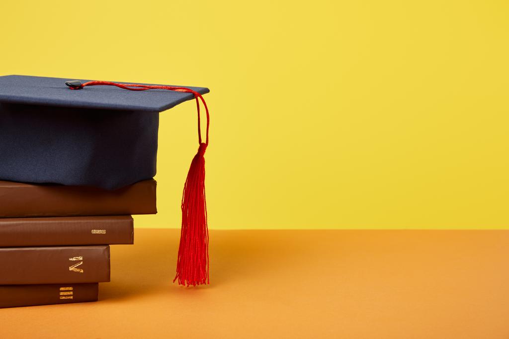 Academic cap and brown books on orange surface isolated on yellow - Photo, Image