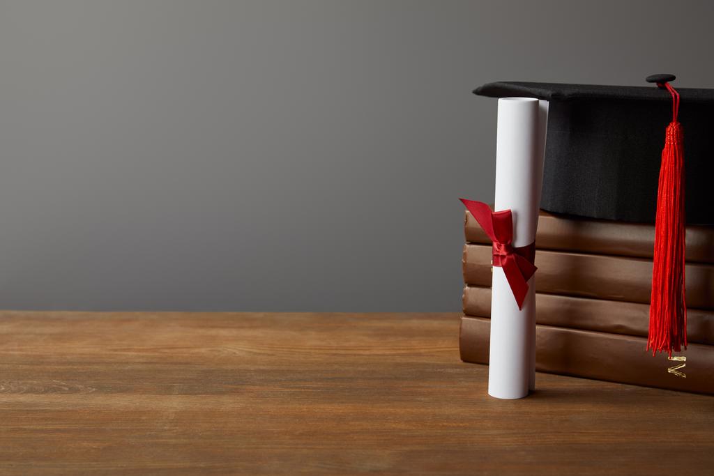 Диплом, академическая шапка и книги по деревянной поверхности изолированы на сером
 - Фото, изображение