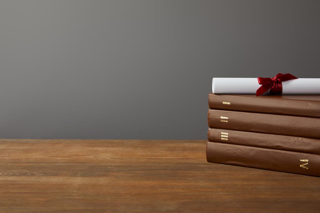 Brązowe książki i dyplom z czerwoną wstążką na drewnianej powierzchni na szaro - Zdjęcie, obraz