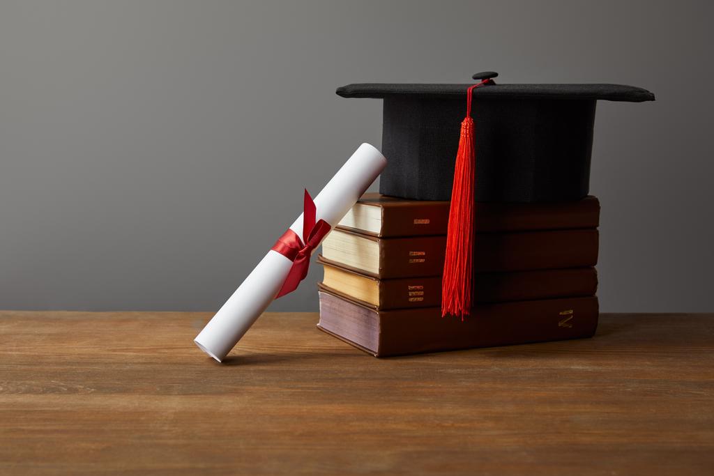 Diploma, academic cap and books on wooden surface isolated on grey - Photo, Image