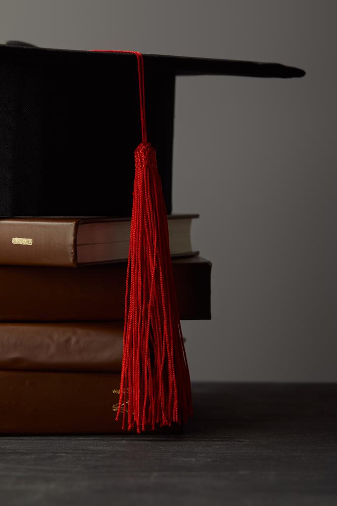 Libri marroni e berretto accademico con nappa rossa isolata su grigio
 - Foto, immagini