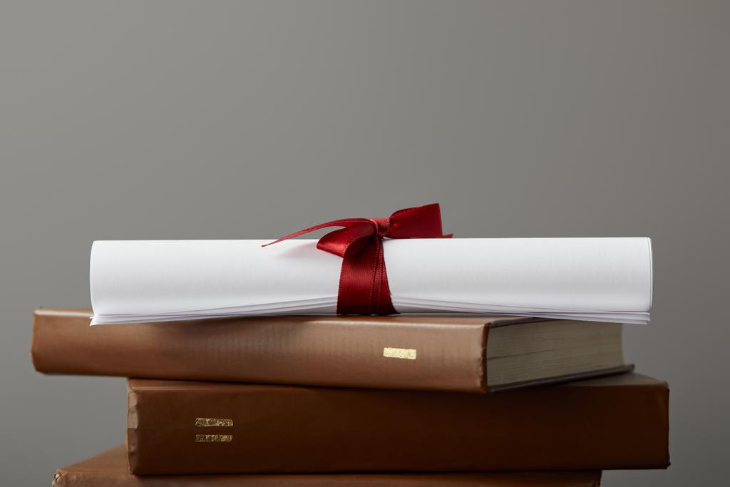 Brown books and diploma with red ribbon isolated on grey - Photo, Image