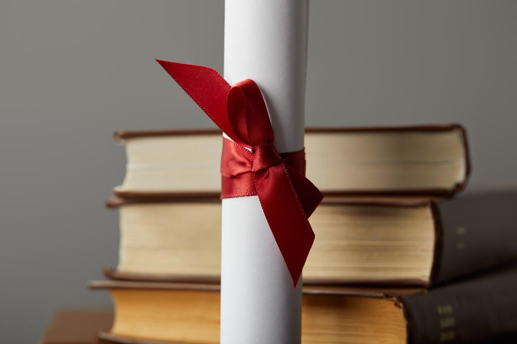 Diploma com fita vermelha e livros isolados em cinza
 - Foto, Imagem