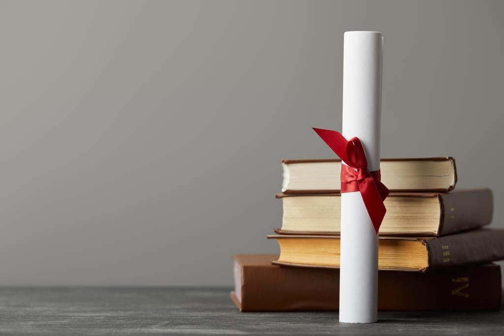 Diploma met rood lint en boeken op gestructureerd oppervlak geïsoleerd op grijs - Foto, afbeelding