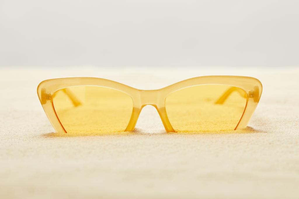selektiver Fokus der gelben Sonnenbrille in goldenem Sand isoliert auf grau - Foto, Bild