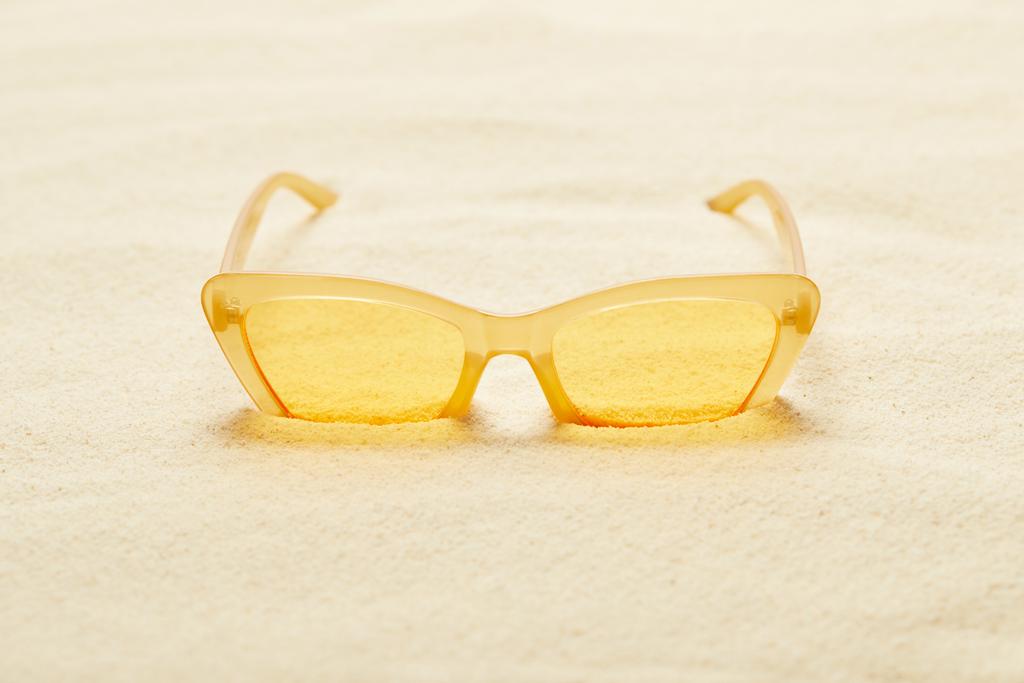 επιλεκτική εστίαση των κίτρινων γυαλιών ηλίου στην αμμώδη παραλία το καλοκαίρι   - Φωτογραφία, εικόνα