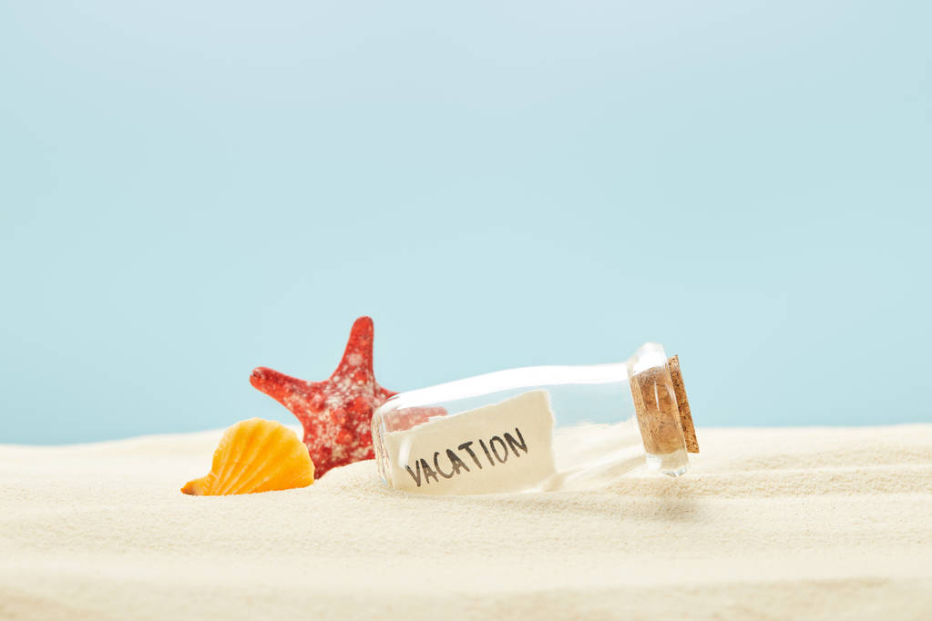 glass bottle with vacation lettering on paper near seashell and starfish isolated on blue - Photo, Image