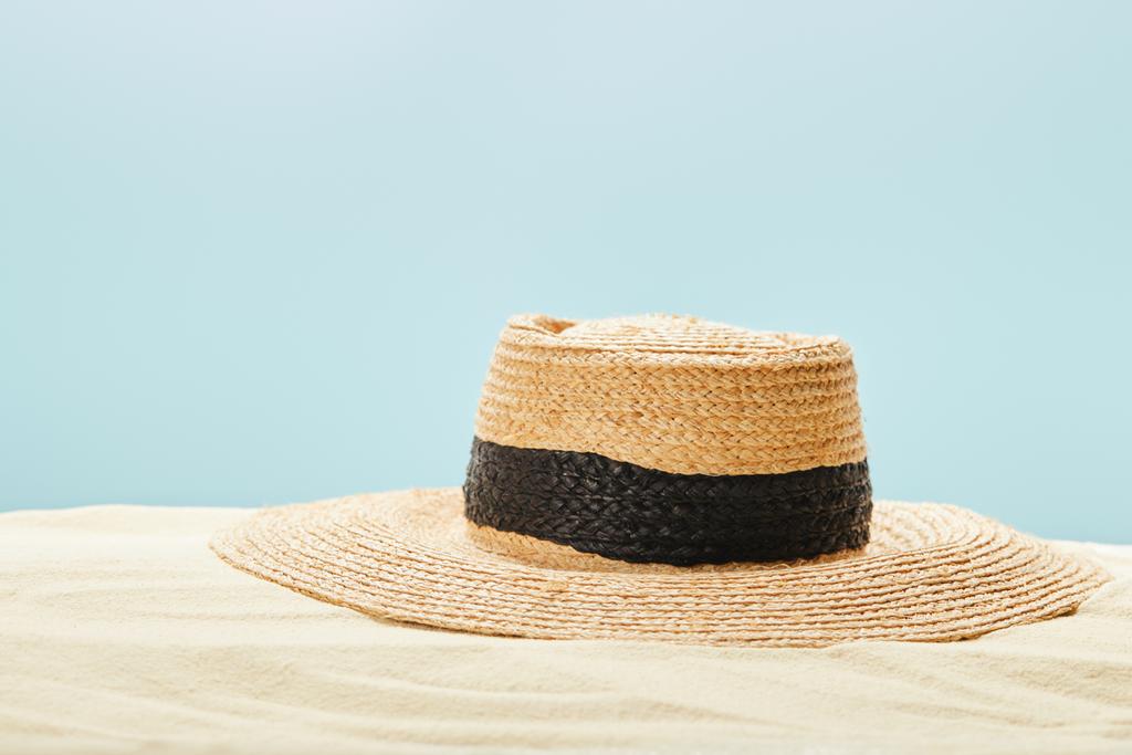 selective focus of straw hat on sandy beach in summertime isolated on blue - Photo, Image