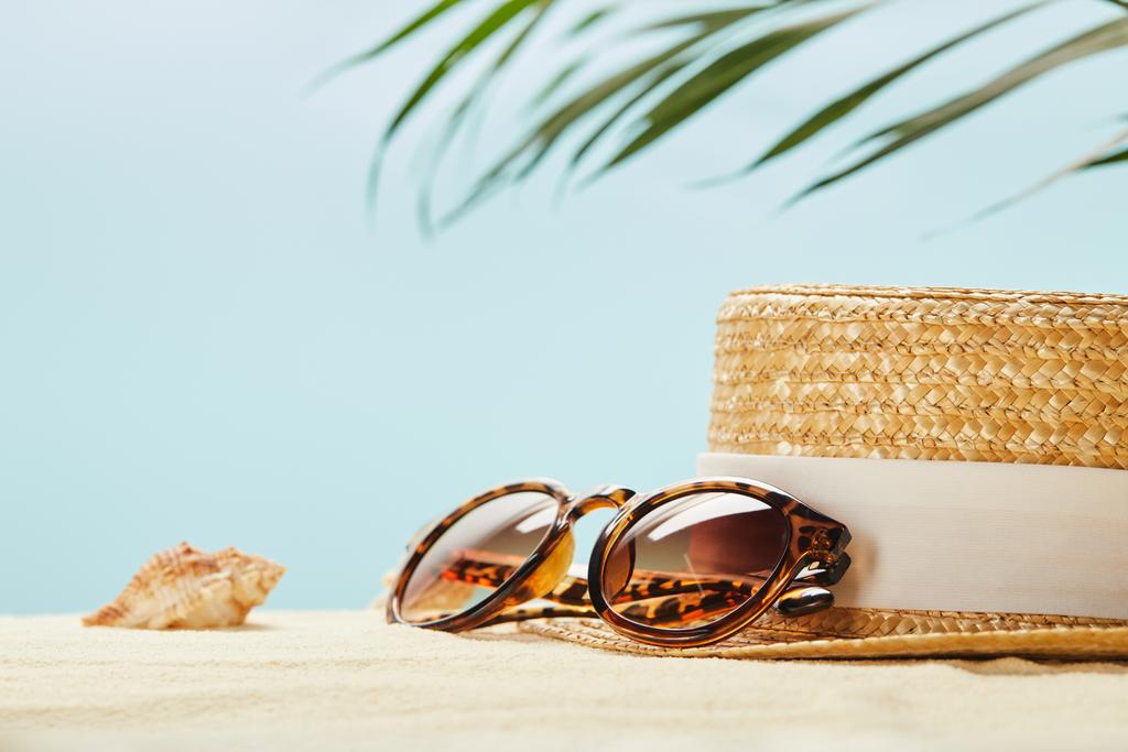 enfoque selectivo de gafas de sol cerca de sombrero de paja y concha en verano aislado en azul
 - Foto, Imagen