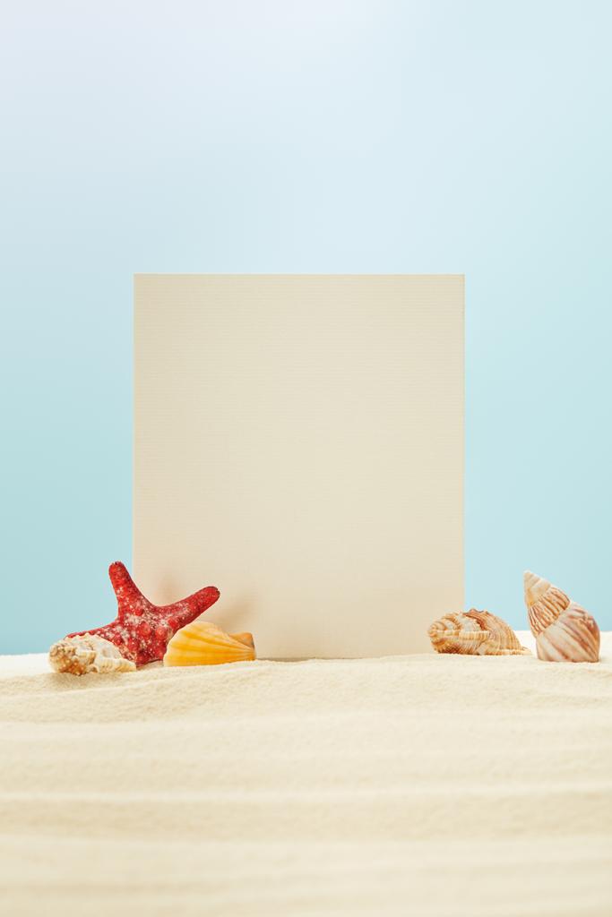 red starfish and seashells near blank placard on sand isolated on blue - Photo, Image