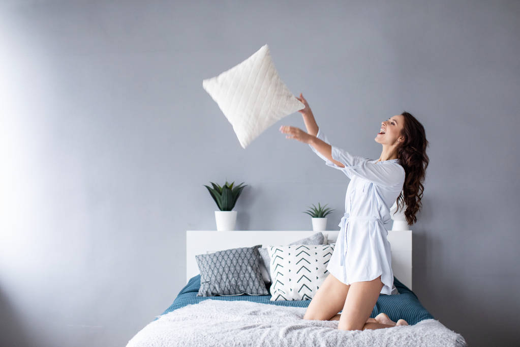 Happy woman having fun pillow throws enjoying funny activity on weekend at home.  - Photo, Image