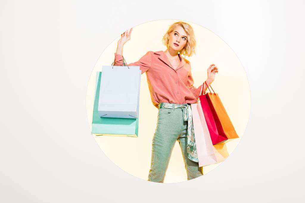 schönes stylisches Mädchen posiert mit Einkaufstaschen auf weiß mit gelbem Kreis - Foto, Bild