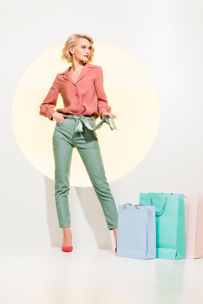 beautiful fashionable girl posing near shopping bags on white with yellow circle - Photo, Image