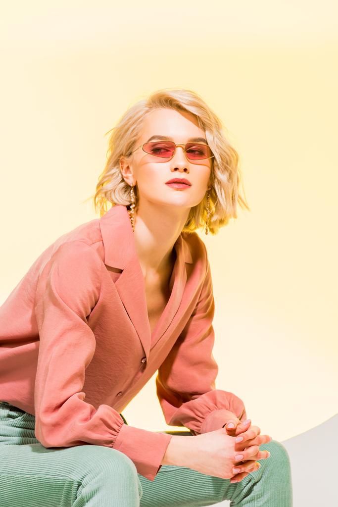 beautiful stylish girl in coral jacket and sunglasses posing on yellow  - Photo, Image