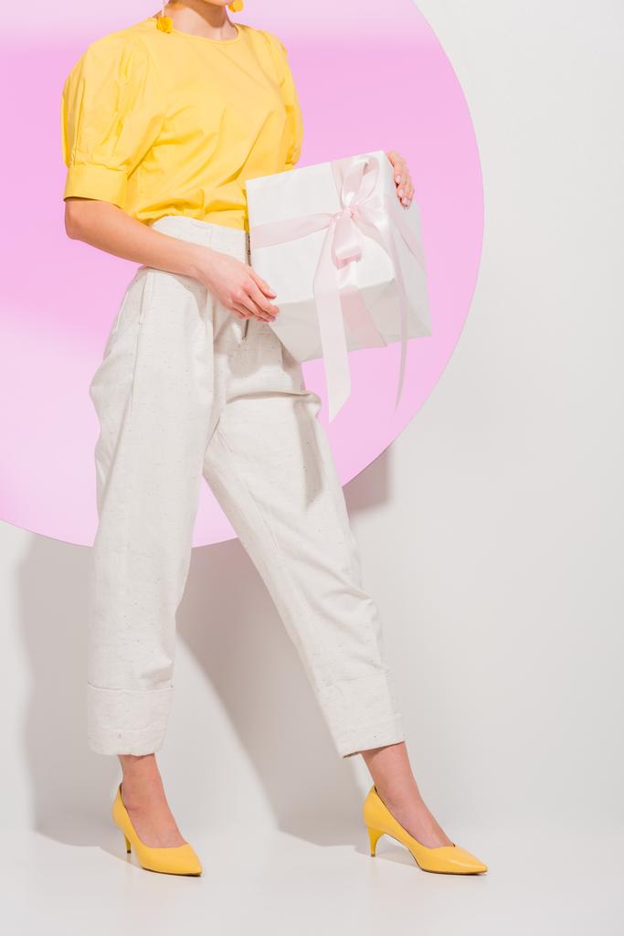 bijgesneden weergave van stijlvolle meisje Holding geschenkdoos op wit met roze cirkel - Foto, afbeelding