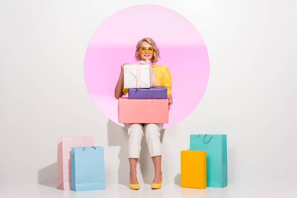 belle fille à la mode posant avec des boîtes de cadeau colorées et des sacs à provisions sur le blanc avec le cercle rose - Photo, image