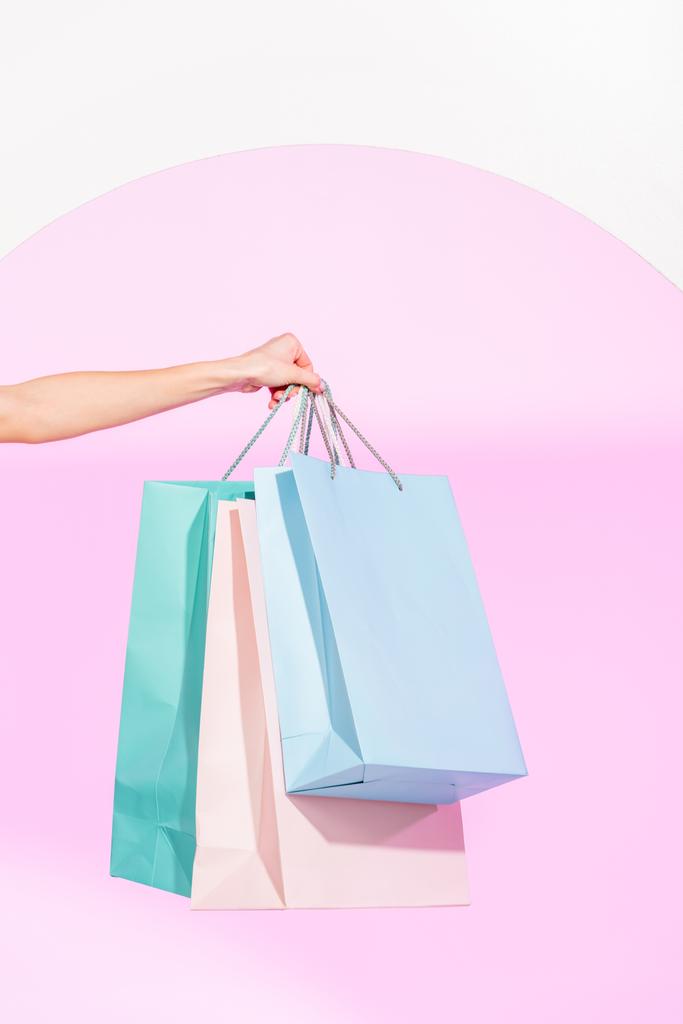 cropped view of young woman holding colorful shopping bags on white with pink circle - Photo, Image