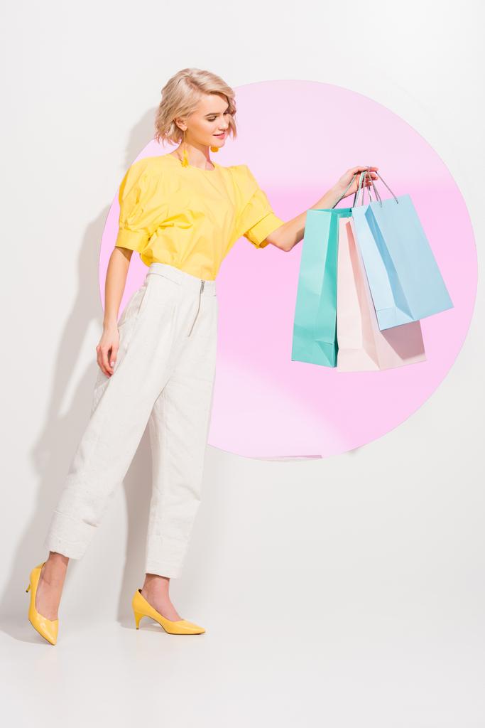 schöne stylische junge Frau mit bunten Einkaufstaschen auf weiß mit rosa Kreis - Foto, Bild