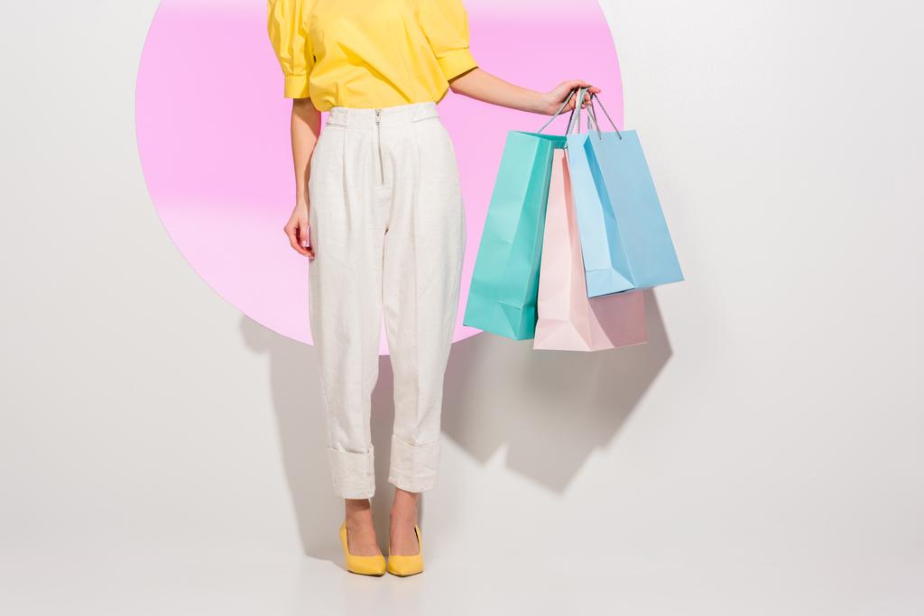 gedeeltelijke weergave van stijlvolle meisje bedrijf kleurrijke boodschappentassen op wit met roze cirkel - Foto, afbeelding