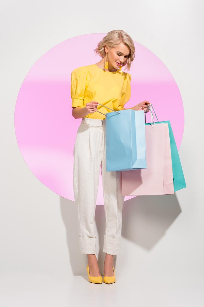 hermosa chica elegante sosteniendo coloridas bolsas de compras en blanco con círculo rosa
 - Foto, imagen