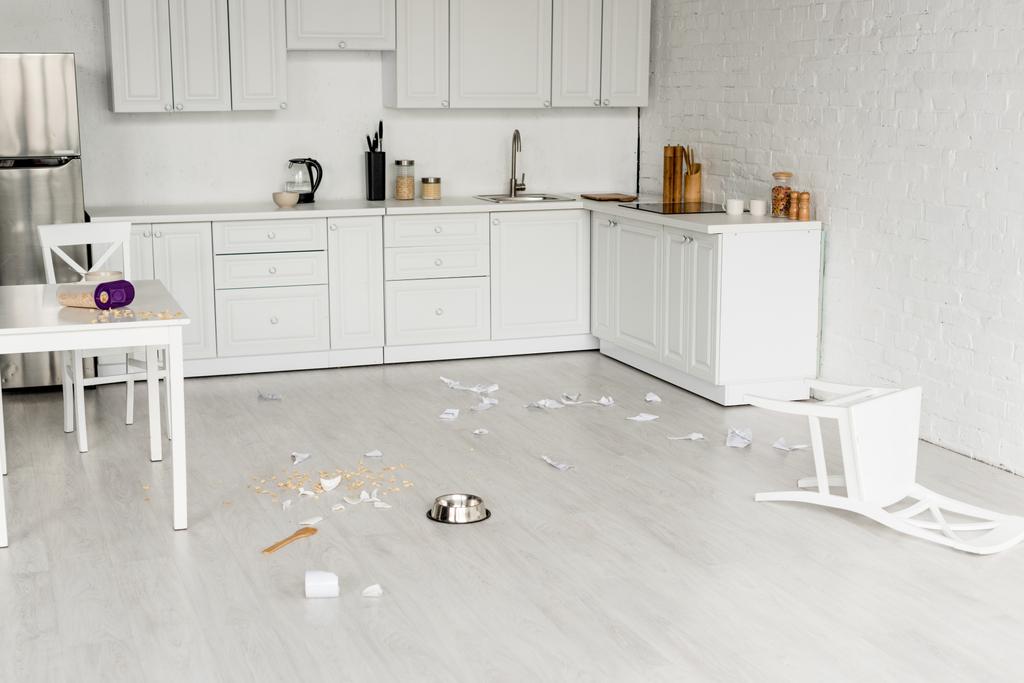 interno della cucina con ciotola di metallo, cucchiaio di legno e piatti rotti sul pavimento
  - Foto, immagini
