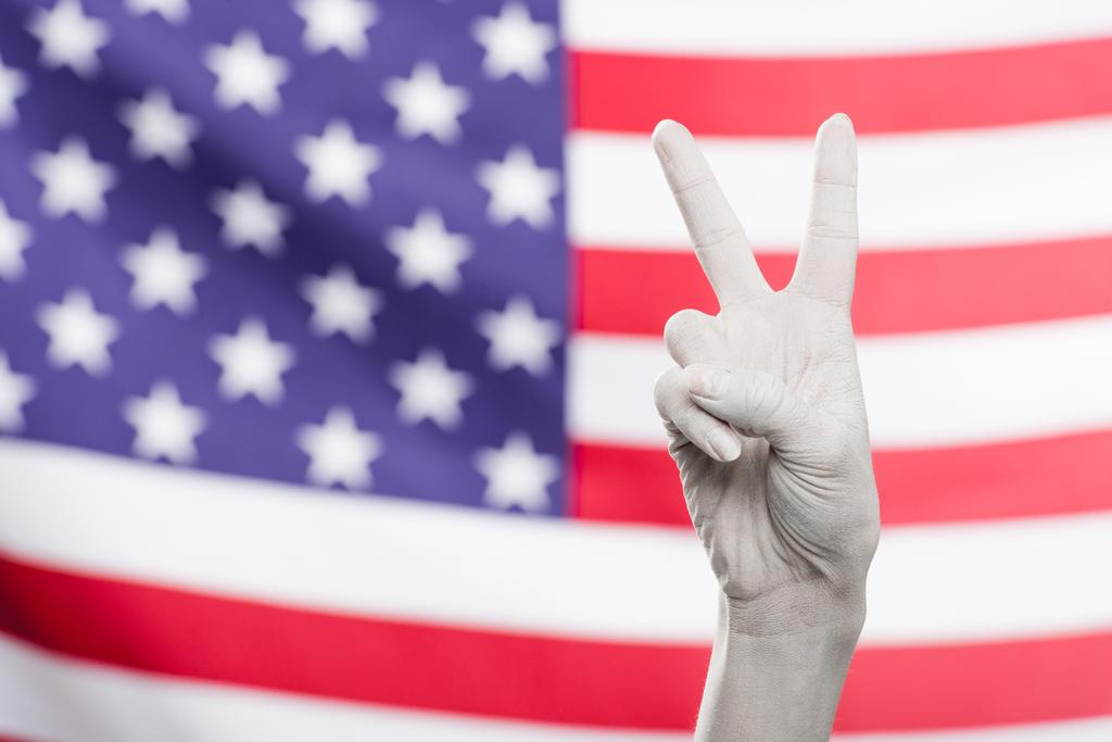 abgeschnittene Ansicht einer weiß bemalten weiblichen Hand, die ein Friedenszeichen in der Nähe der amerikanischen Flagge zeigt  - Foto, Bild
