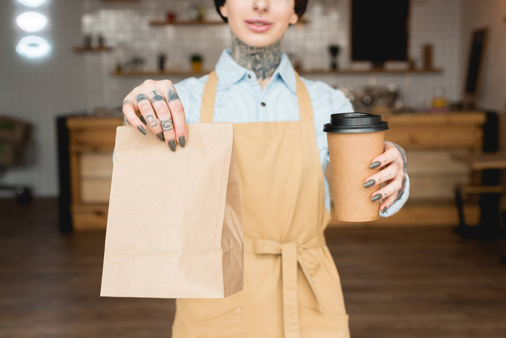 partial view of waitress holding paper bag and disposable cup in outstretched hands - Photo, Image
